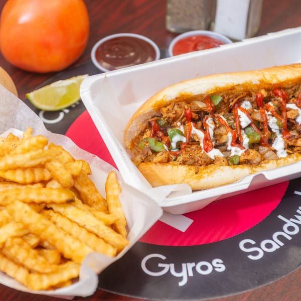 A chicken cheesesteak sandwich with fries, ketchup, BBQ sauce, a tomato, onion, and lime.