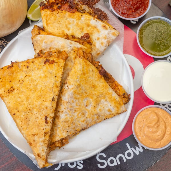 Golden-brown quesadillas on a white plate, with four dipping sauces and a lime wedge.