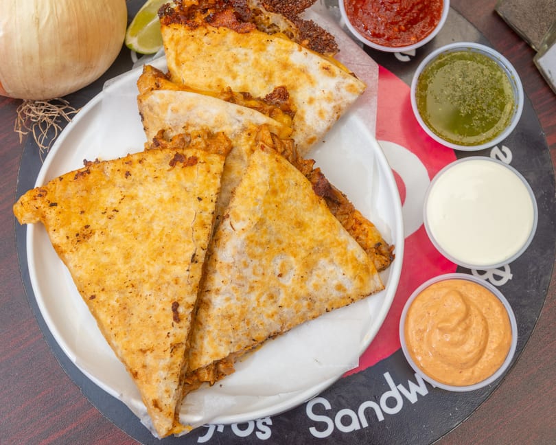 Golden-brown quesadillas on a white plate, with four dipping sauces and a lime wedge.