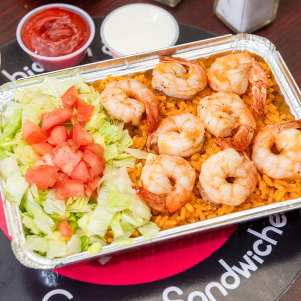 Shrimp and rice platter with lettuce and tomatoes, served with ketchup and white sauce.