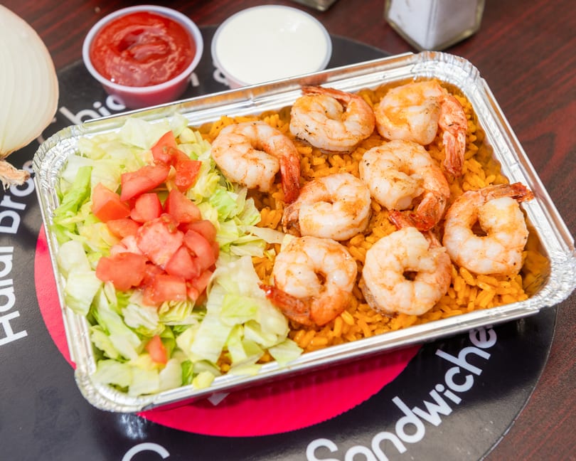 Shrimp and rice platter with lettuce and tomatoes, served with ketchup and white sauce.