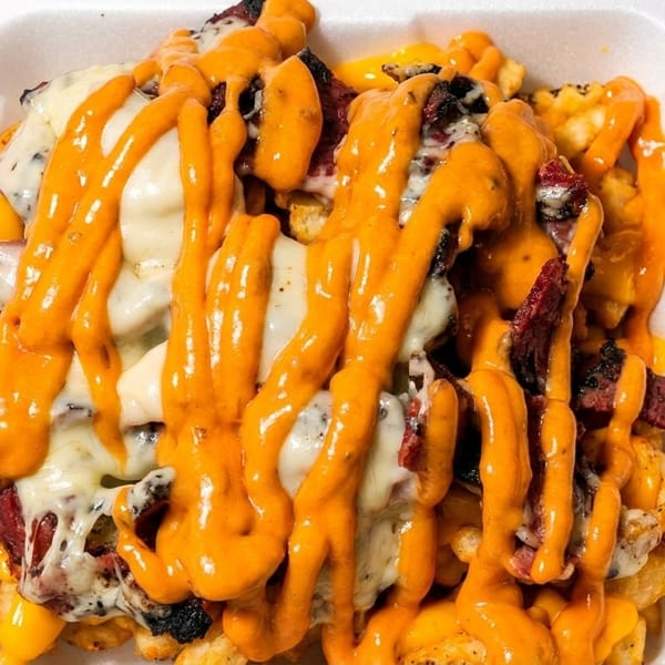 Loaded fries with melted white and yellow cheese, topped with meat and orange sauce in a white container.